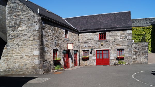 Der Hofplatz in der Blair Athol Whisky Destillerie mit seinen Gebäuden aus grauem Stein und roten Türen und Fenstern.